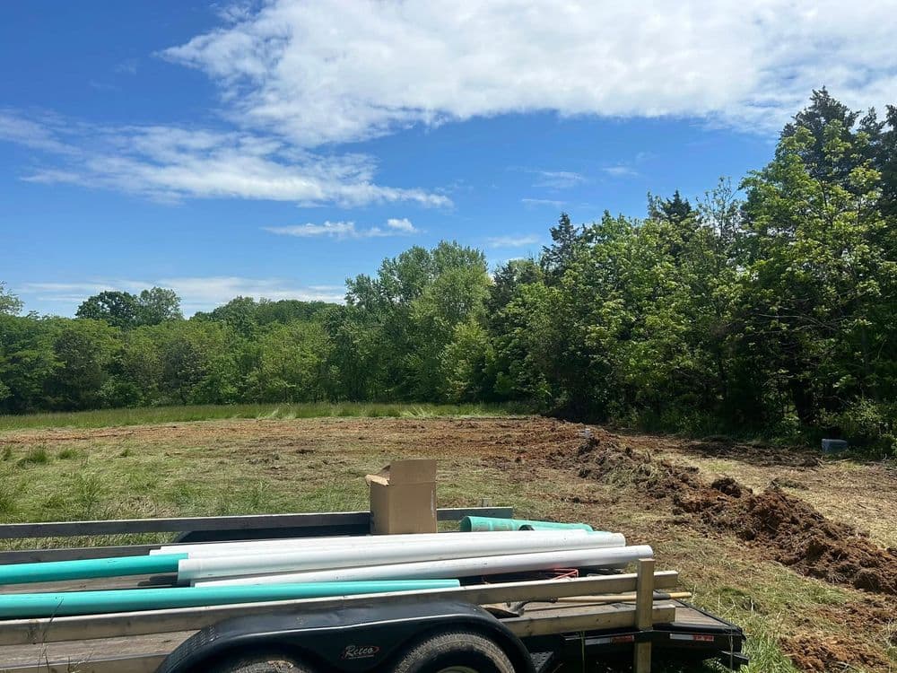 Construction site with PVC pipes on a trailer, surrounded by greenery and clear blue sky.