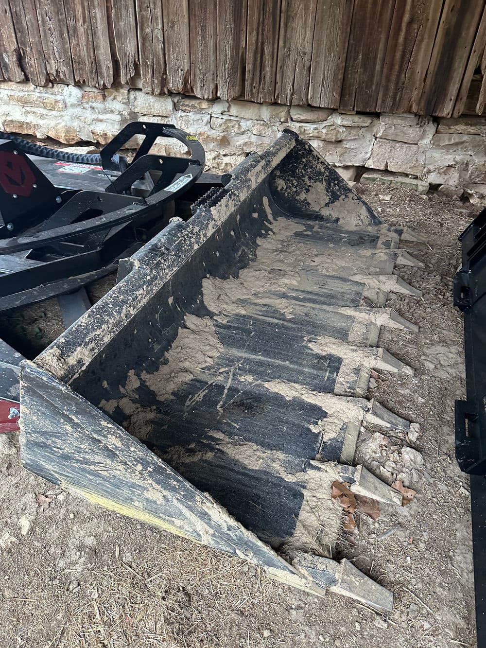Heavy-duty tractor bucket attachment placed on the ground in a barn setting.